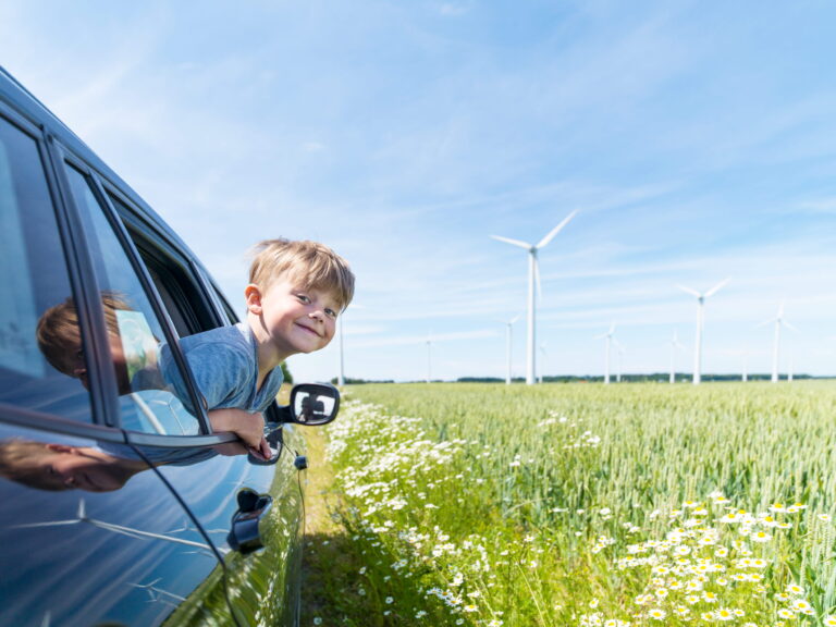 Liten kille tittar ut från fönstret på en bil. BIlen kör bredvid en äng med vindsnurror i bakgrunden.